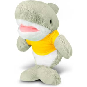A plush shark toy in pale green with a white belly and a yellow T-shirt, featuring a brand logo.