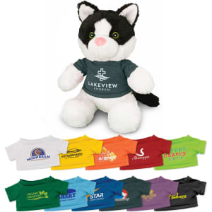 A soft black and white cat plush toy wearing a green T-shirt with a logo. Multiple other T-shirts in various colours are arranged below.