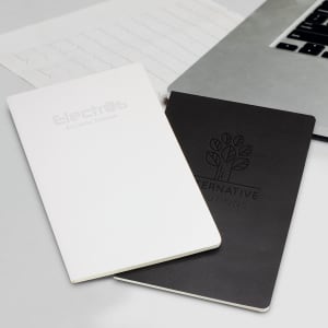 Two Moleskine Volant journals, one white and one black, placed beside a laptop and a notepad. Each has a logo on the cover.