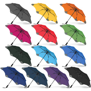 A collection of BLUNT Metro umbrellas in various colours, including black, yellow, orange, pink, red, green, blue, and purple. Each umbrella has a sleek design.