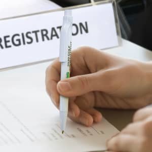 An anti-microbial pen in white is held above a sheet of paper for signing or writing.
