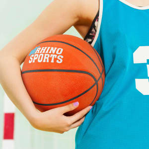 A basketball held by a person wearing a teal sports jersey, featuring a logo and a number. The ball is orange.