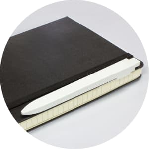 A black notebook with a white pen resting on the edge. The notebook features a textured cover and a band.