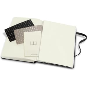 A large hard cover notebook with an elastic closure, featuring blank pages and decorative sheets inside.