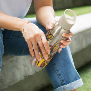 A drink bottle made of aluminium with intricate designs, featuring a beige lid and a metallic finish.