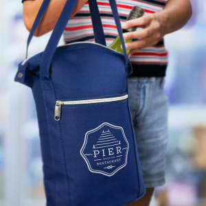 A drink bottle is held next to a navy cooler bag featuring a logo and a zippered pocket.