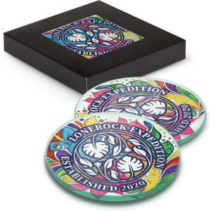 A set of two round glass coasters featuring a colourful design and a branded logo, packaged in a black box.