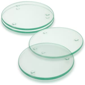 A set of four round glass coasters in pale green, featuring subtle raised dots for stability.