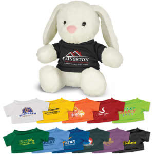 A fluffy white rabbit plush toy wearing a black shirt with a logo, surrounded by various colourful t-shirts.