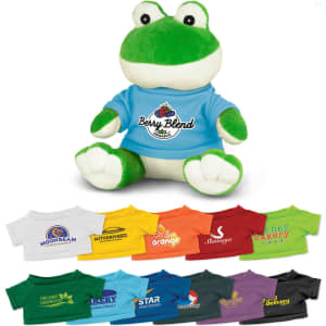 A green frog plush toy wearing a blue shirt, surrounded by various colourful t-shirts in different shades.