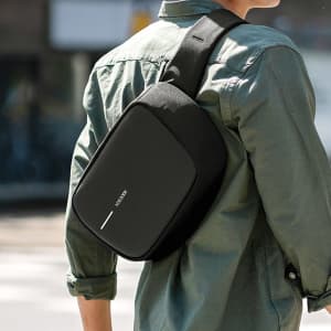 A black sling bag is worn across a person's shoulder, featuring a sleek design and a logo on the front.