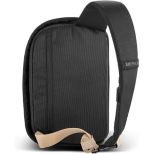 A black sling bag with a tan strap and a zipper pocket, featuring a logo on the strap.