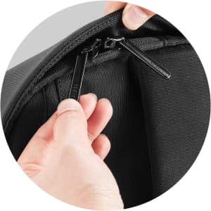A black zippered compartment is being opened with two black zipper pulls. The fabric appears durable and textured.