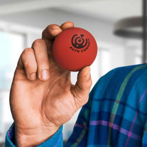 A hand holds a red Hi-Bounce Ball featuring a logo, set against a blurred indoor background.