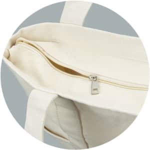 A cream-coloured canvas tote bag with a zipped compartment and sturdy handles. It features a subtle logo.