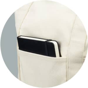 A cream canvas tote bag with a black notebook tucked into a side pocket. The bag features a logo.