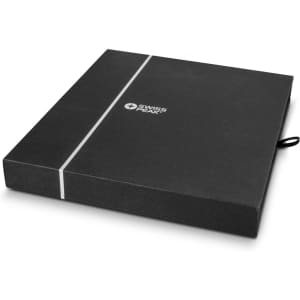 A black presentation box with a ribbon, containing a notebook and pen set. The box features a branding logo.