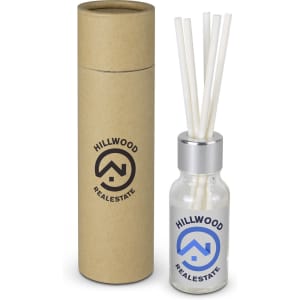 A glass scented diffuser in a cylindrical cardboard container, featuring a logo, with white reeds for fragrance dispersal.