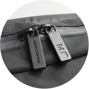 A zip detail of a black Moleskine Metro Slim Backpack featuring dual zippers and a textured surface.