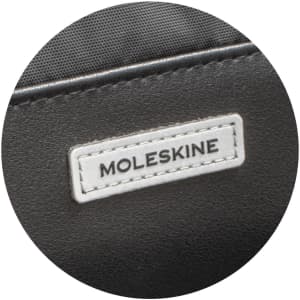 A close-up of a black Moleskine Metro Slim Backpack featuring a white logo tag.