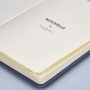 A navy notebook with cream pages, featuring a branding logo on the interior page.