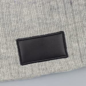 A grey cable knit beanie featuring a black patch, made from soft wool blend material.