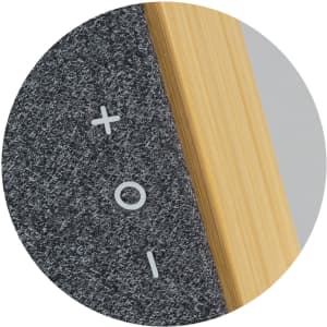 A close-up of a grey Bluetooth speaker featuring a bamboo detailing and volume control buttons.
