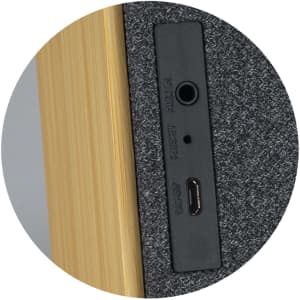 A close-up of the back of a grey and wooden Bluetooth speaker, featuring ports for audio and charging.