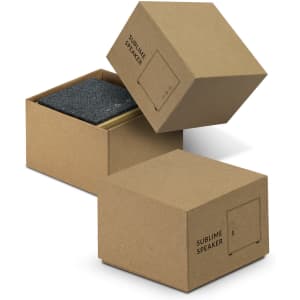 A grey Bluetooth speaker in a cardboard box, featuring a simple design with a logo on the side.