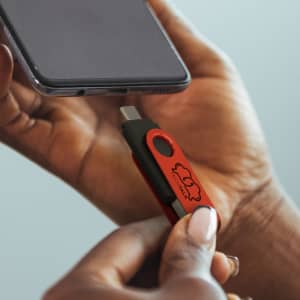 A red and black dual flash drive being inserted into a smartphone, featuring a logo on the drive.