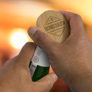 A bamboo bottle opener held in a hand, featuring a circular design and engraved text. The background is softly blurred.