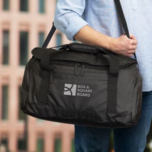 A black duffle bag with a shoulder strap, featuring a logo on the front, held by a person.