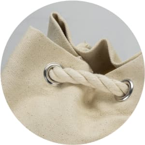 A beige canvas barrel bag with metal eyelets and a twisted rope handle, featuring a simple, unadorned design.