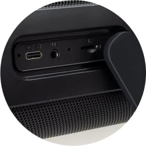 A close-up of a black Bluetooth speaker showcasing USB-C, AUX, and TF card ports. The speaker features a textured surface.