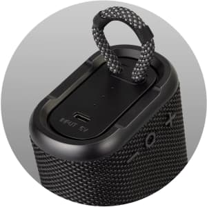 A black outdoor Bluetooth speaker with a textured surface and a carrying loop on top. It features a USB input.