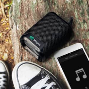 A black outdoor Bluetooth speaker with a textured surface and a logo, placed on a wooden surface beside a smartphone.