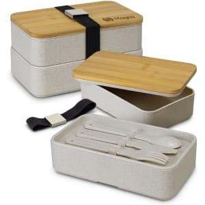A stackable lunch box in beige with bamboo lids, featuring utensils and a black strap for closure. It has a logo on the front.