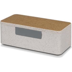 A wireless charger and speaker combination in off-white with a cork top and a grey button. It features a minimalist design.