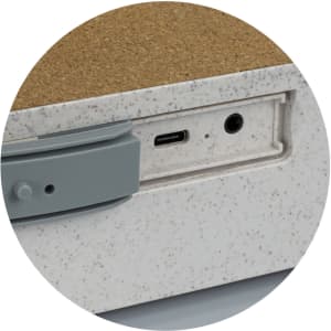 A close-up of a wireless charger with a textured surface, featuring a USB-C port and a headphone jack in grey.