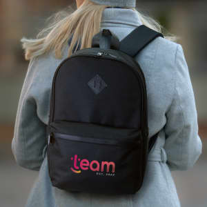 A black backpack worn on a person's back, featuring a logo on the front and adjustable shoulder straps.