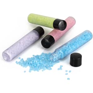 A set of four containers of bath salts in blue, pink, green, and purple, with black caps, one spilling salts.