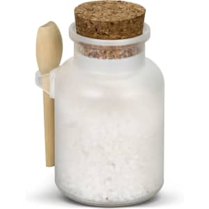 A frosted glass jar filled with white bath salts, topped with a cork lid and a small wooden spoon.
