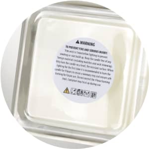 An ambient scented candle in a clear container, featuring a warning label and a white wax interior.