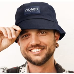 A navy bucket hat with a patch logo is worn by a smiling individual. The hat features a wide brim.