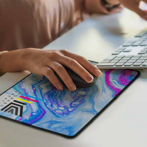 A colourful mouse mat featuring a blue and pink swirling design, with a hand using a black computer mouse on it.