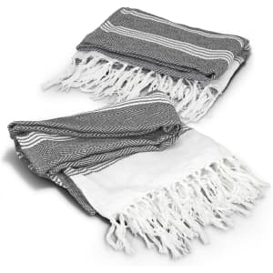 A grey and white Ohau Throw Blanket with tasselled edges, featuring a geometric pattern. It has a branding logo.