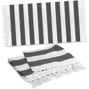 A striped black and white cotton towel with tassels, featuring a flat and folded design.
