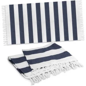 A striped Okana cotton towel in navy blue and white, featuring fringed edges, displayed flat and folded.