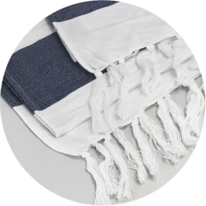 A cotton towel in navy blue and white with fringed edges, featuring a textured design and a logo.