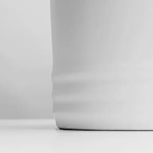 A white coffee mug with a smooth finish and subtle ribbed detailing at the base.